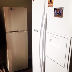 Our small fridge waving goodbye from the shadows of the newer bigger one. 